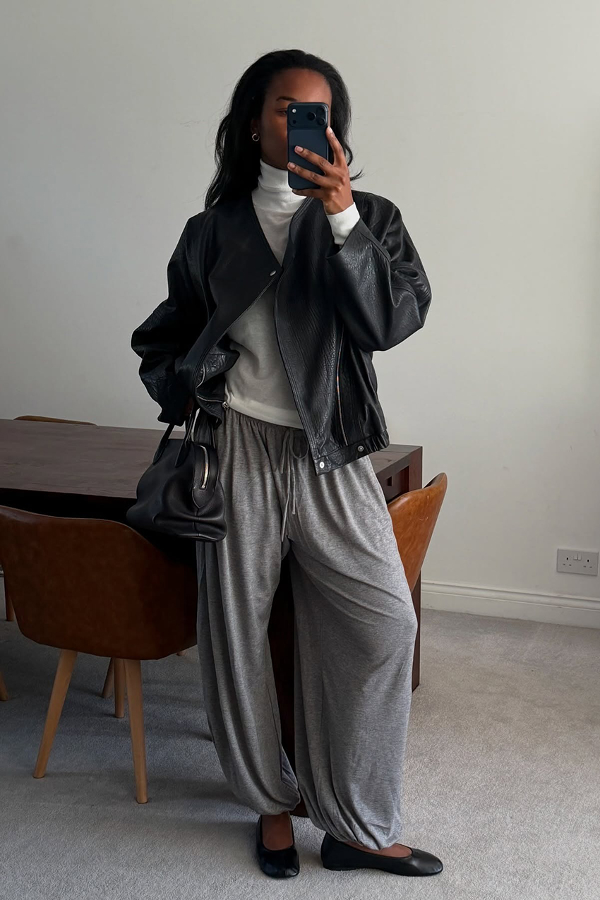 a woman wearing a black leather jacket, white longsleeve top, gray genie pants, and black glove flats