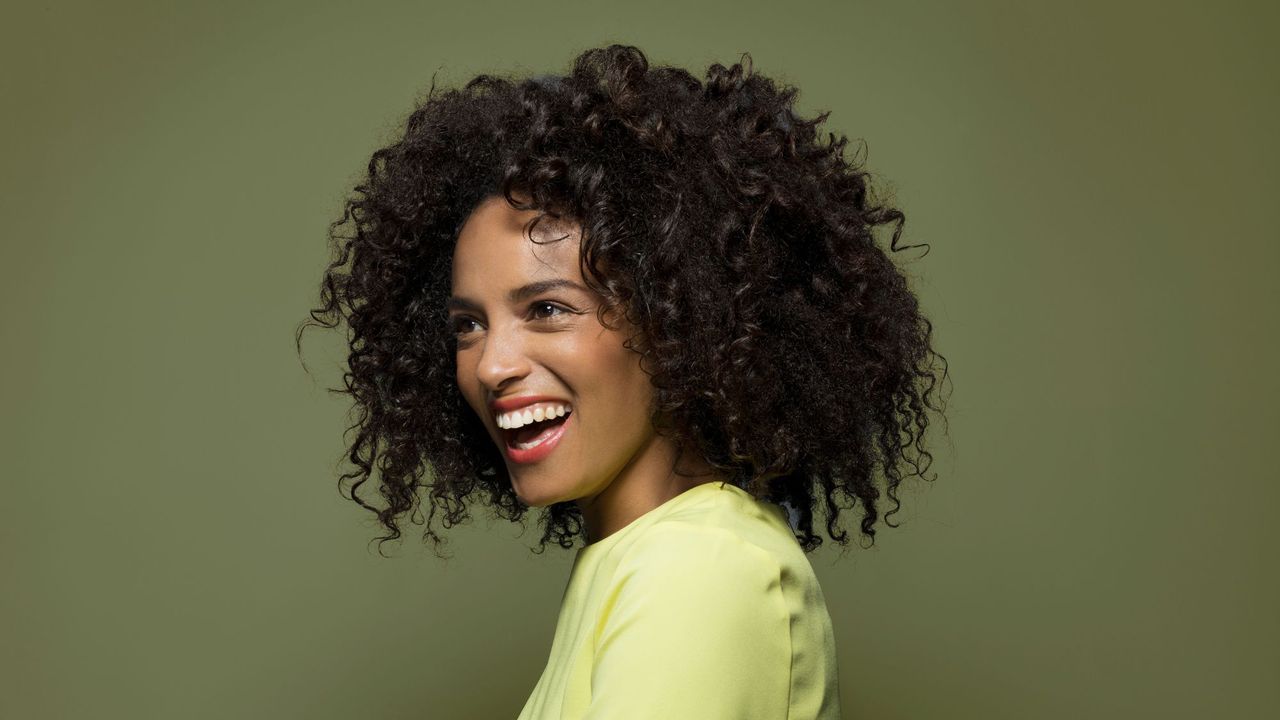 best shampoo for curly hair - woman with beautiful curls smiles with green background - gettyimages 528770243