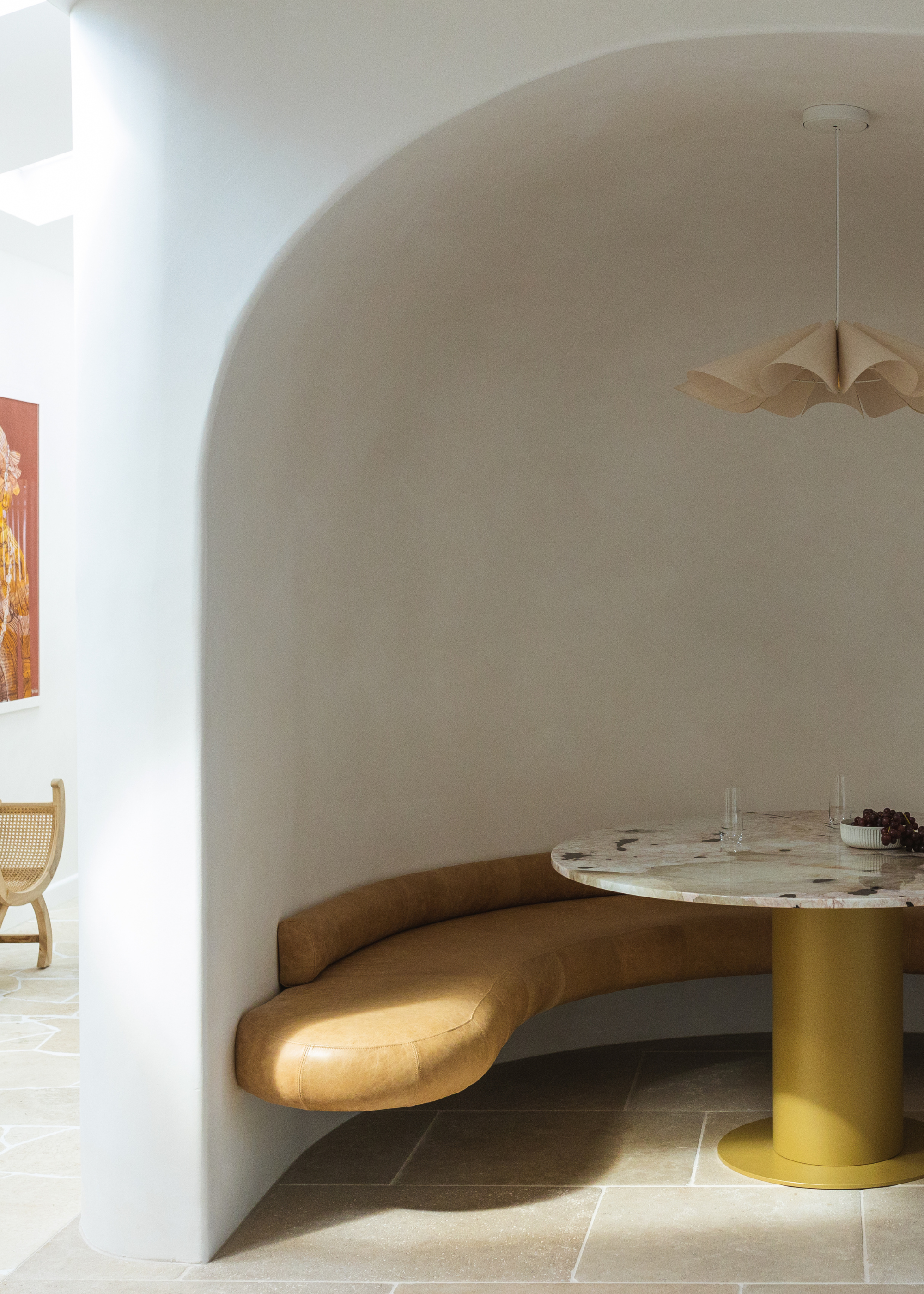 A curved dining nook with a pleated pendant light, a wall-side bench, and a circular stone table in the middle