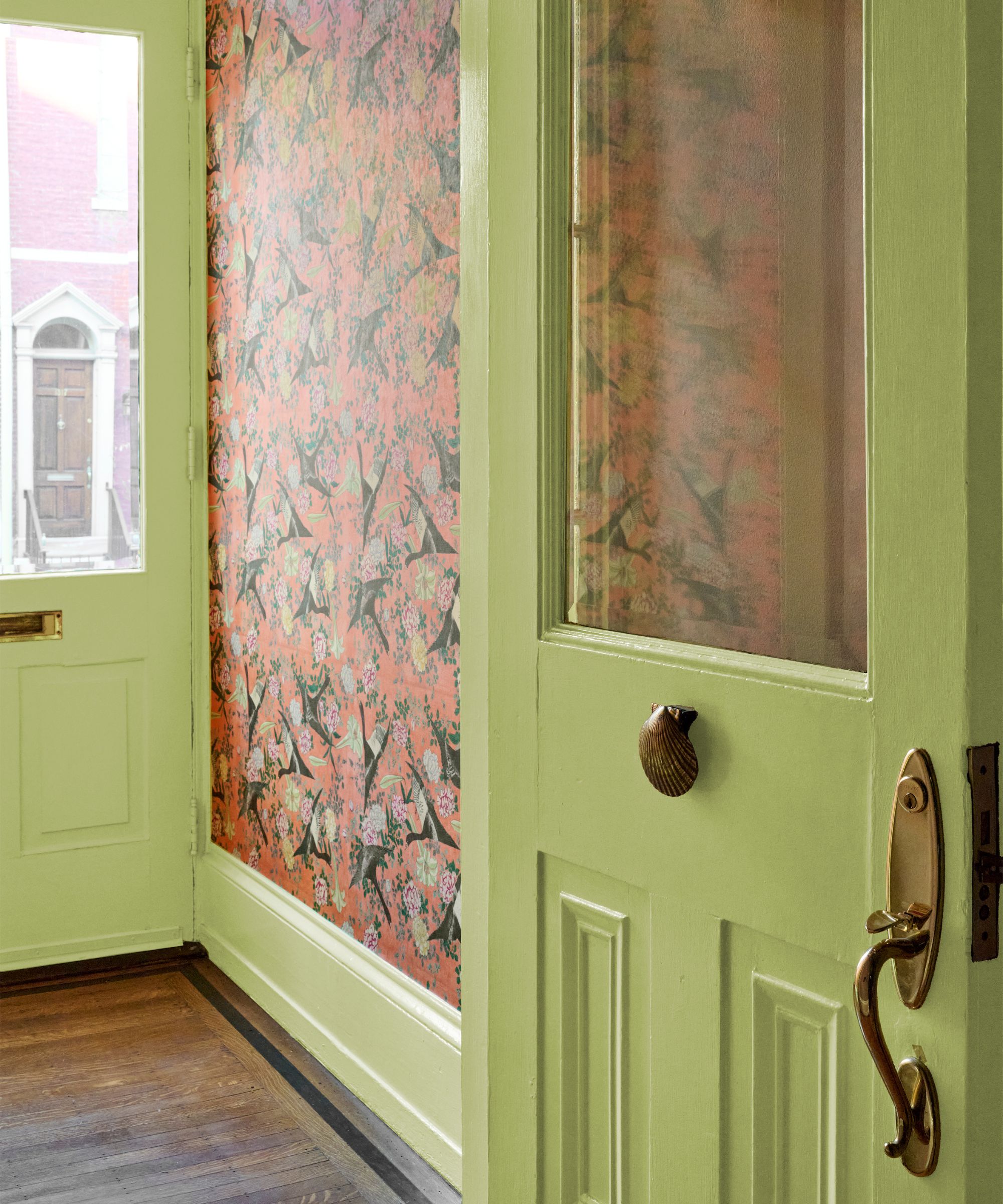 Entryway featuring chartreuse green painted doors, brass shell hardware, and vibrant coral wallpaper with a bird pattern.