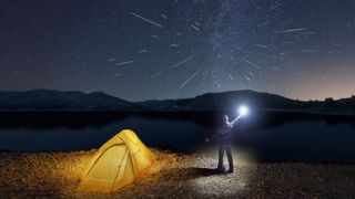 A man with a flashlight and yellow tent watches the Perseid meteor shower