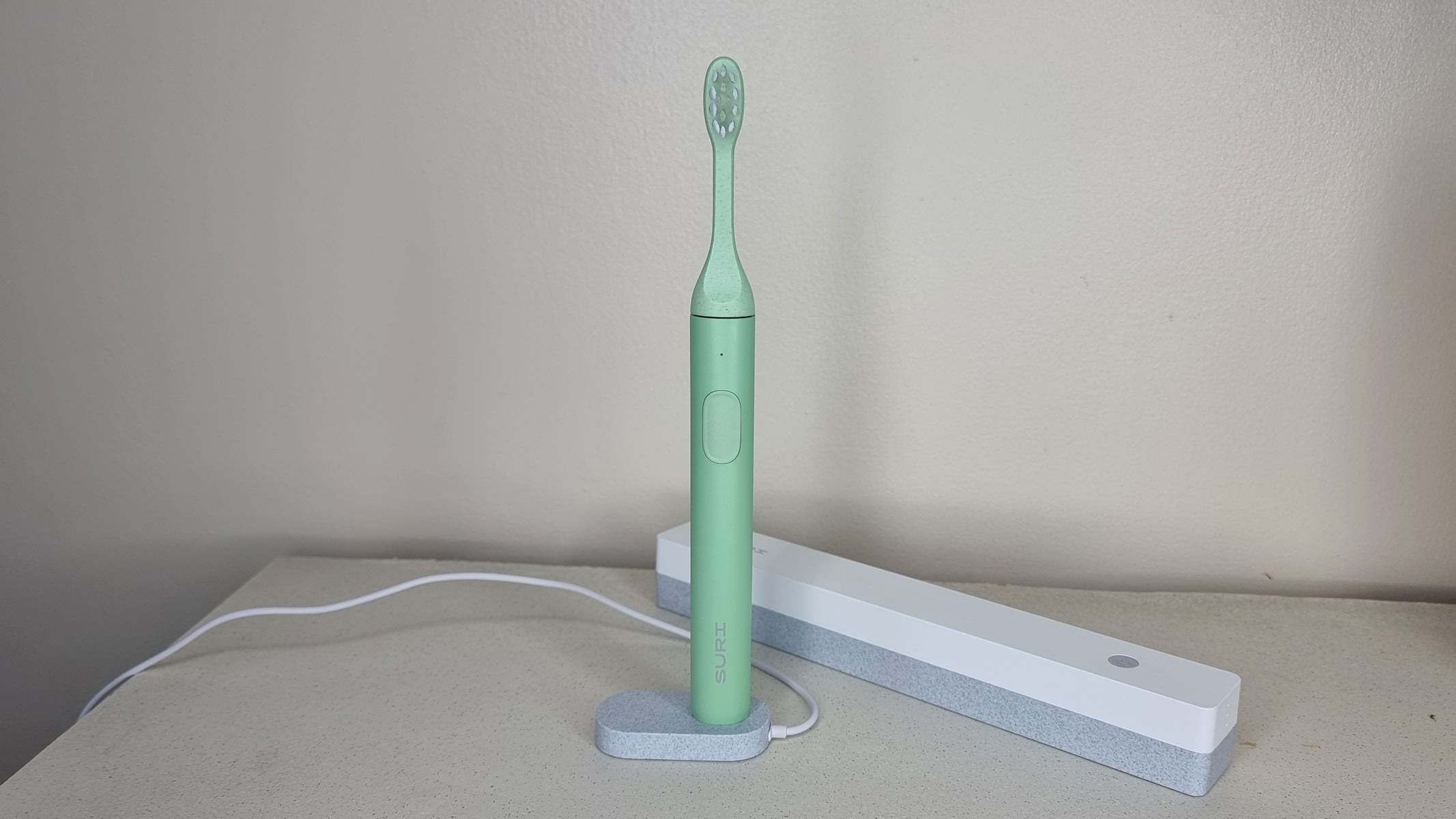 Suri sustainable electric toothbrush standing on a charging pod, with UV-C travel case laying behind them