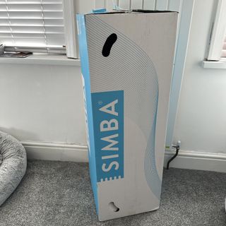 The Simba Hybrid Topper in a branded box in a room with grey carpet