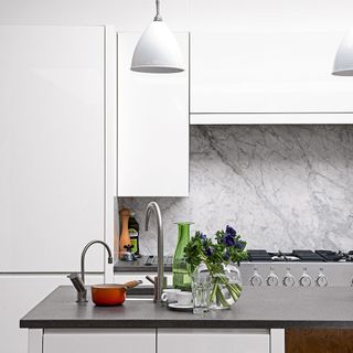 A white kitchen with a marble splashback and pendant lights