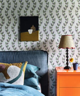 A bedroom with green patterned wallpaper, a bright orange side table and a dark blue-green bedframe