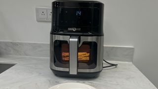 A Paris Rhone Air Fryer on a marble countertop with asparagus in the closed, lid-up drawer