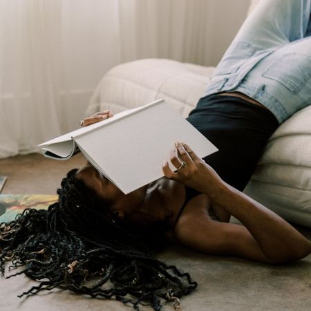 A woman reading a book off the edge of a bed