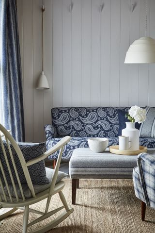 Nautical style living room with white shiplap wall panels, blue patterned couch and upholstered fabric foot stool