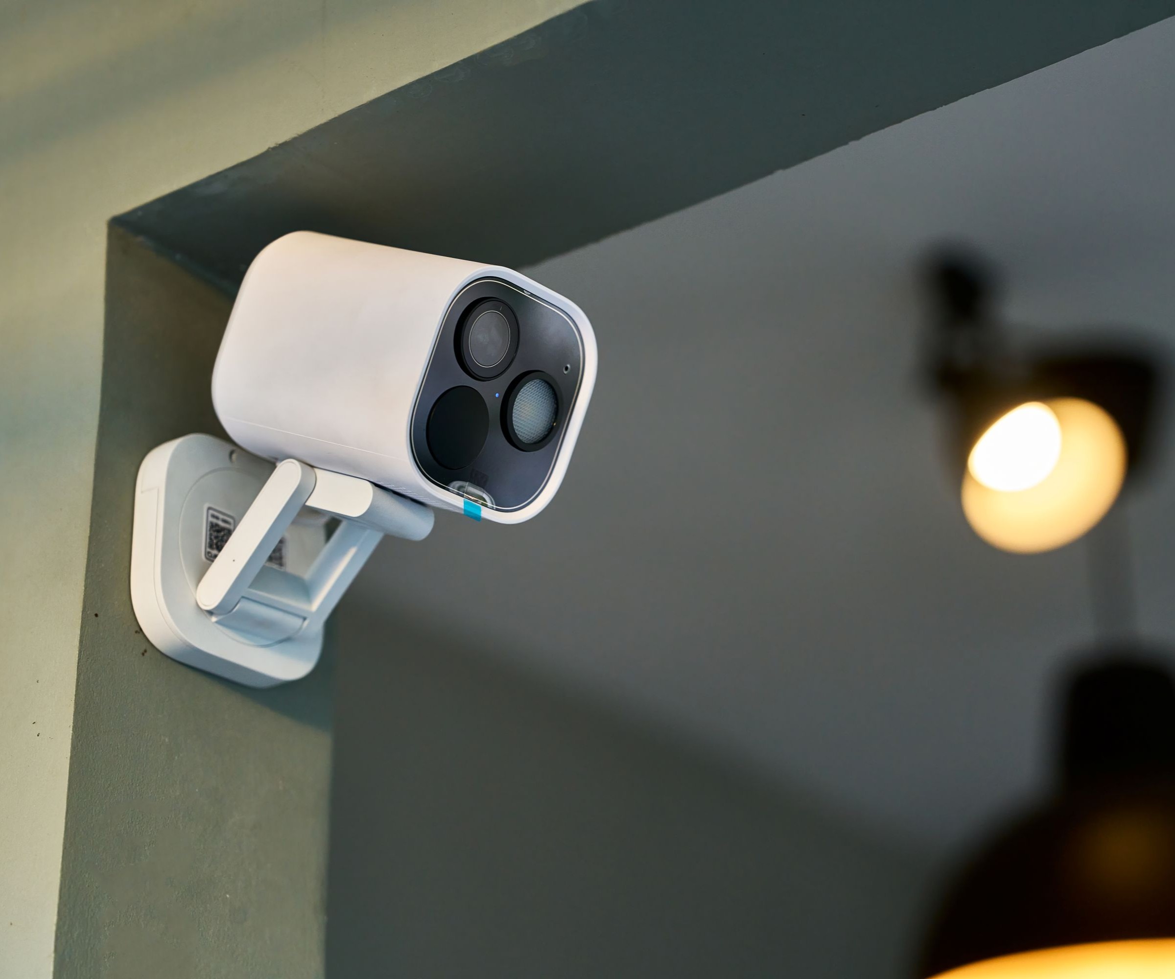 A white security camera affixed to a green wall