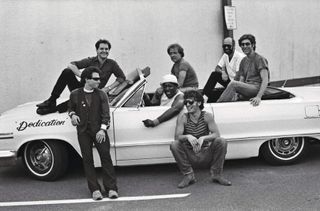 The E Street Band relaxing next to a convertible car