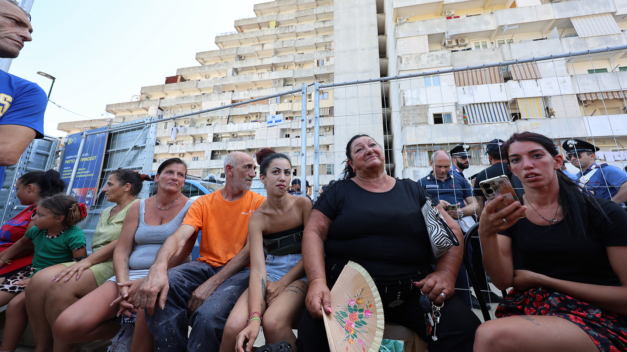 A group of people sit next to a fence in a city center.