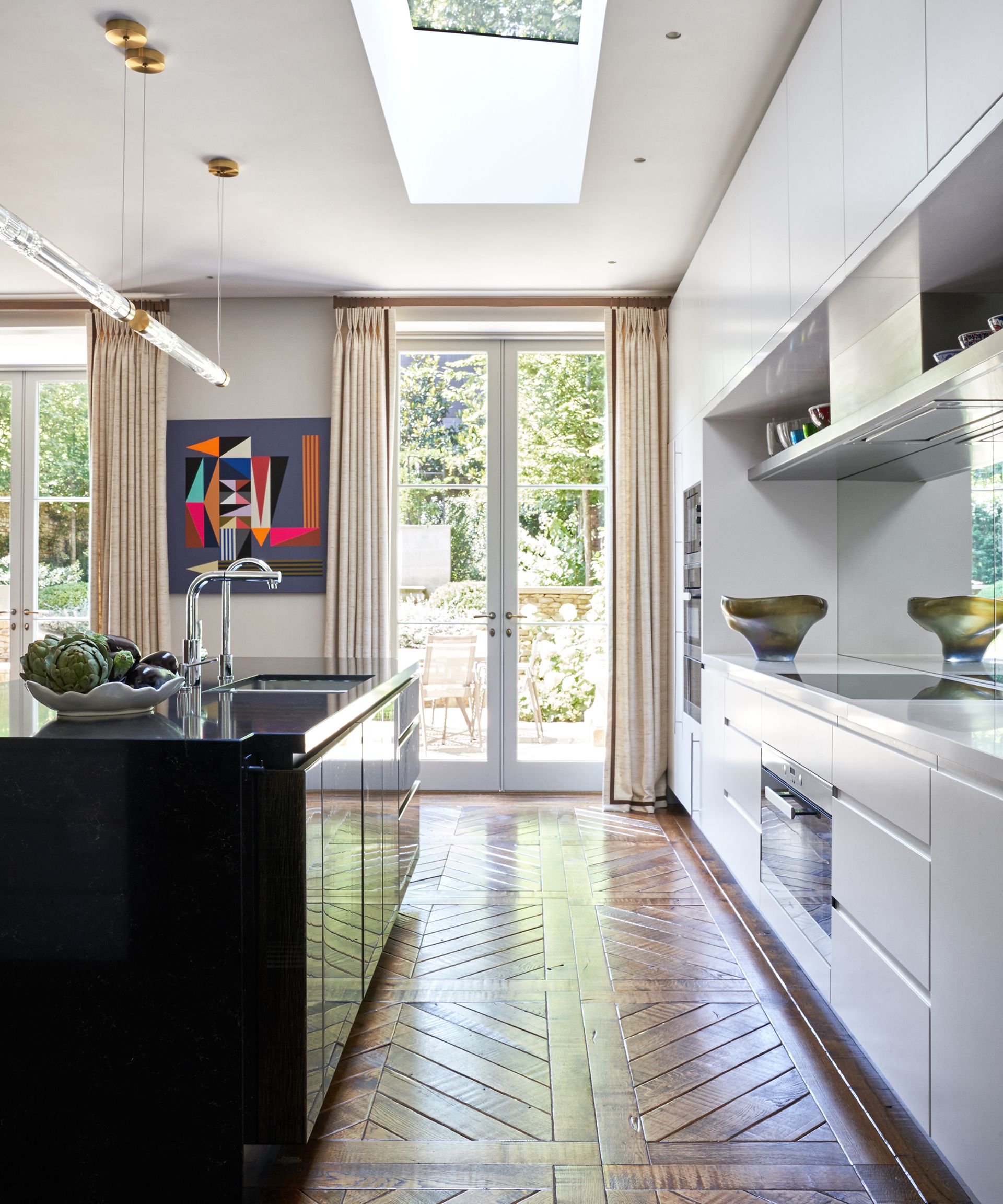 An example of how much does a new kitchen cost showing a white kitchen with a black island and wooden flooring leading to glass doors
