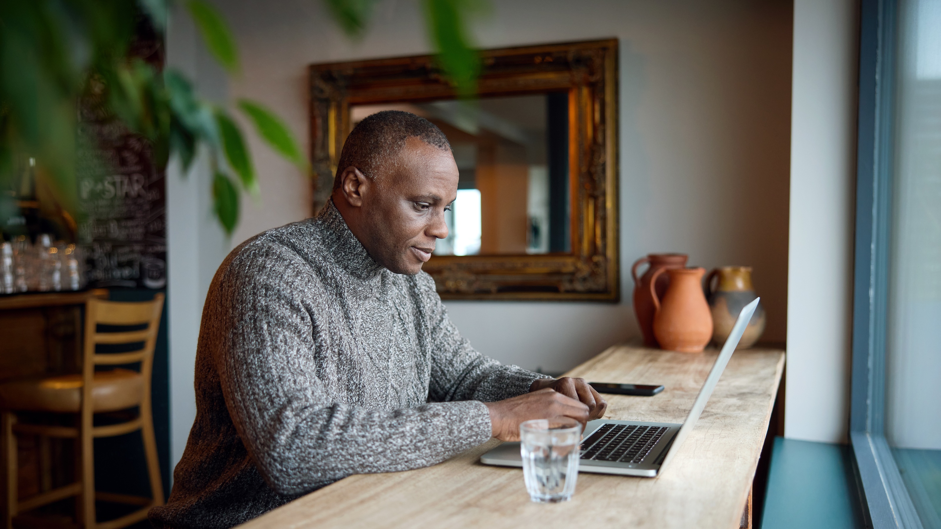 An older man works on a laptop in a cafe.