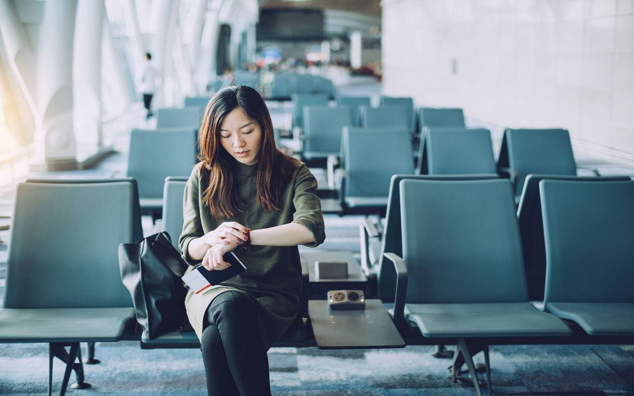 Young businesswoman holding passport and boarding pass on hand, checking wristwatch in airport