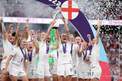 England's Lionesses cheering and holding up their Euros trophy in Wembley Stadium, while Sweet Caroline played in the background
