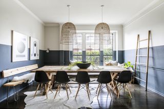 dining room with half painted gray and stone walls, wooden floor, rustic dining table, black chairs, rattan light shades, bench, rug, modern artwork