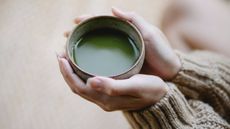 A woman cupping her hands around a mug of matcha, wellness tips