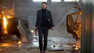 John Wick walks towards the camera with a silenced pistol in his right hand in his first film