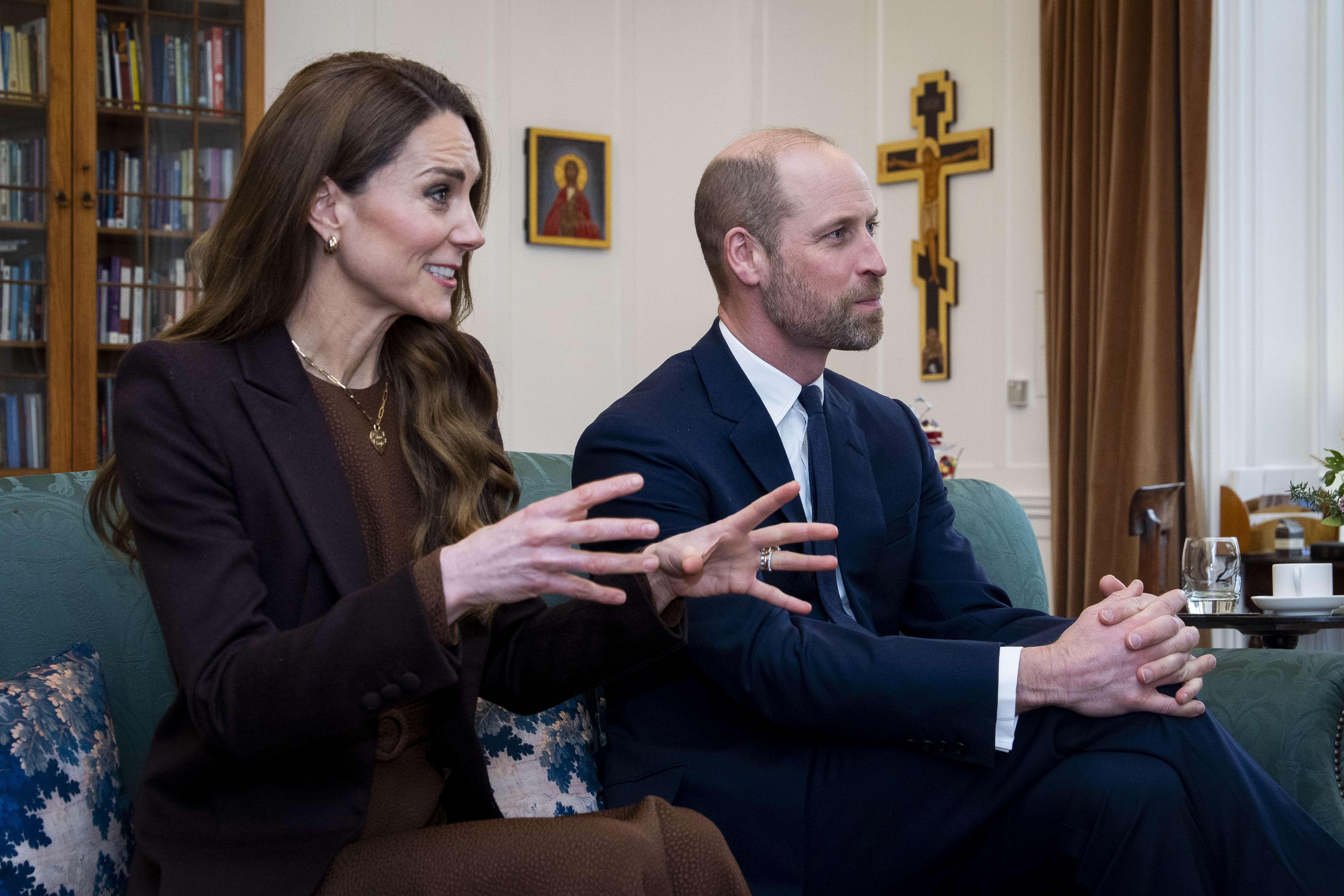 Princess Kate sitting next to Prince William on a couch wearing a brown dress and coat