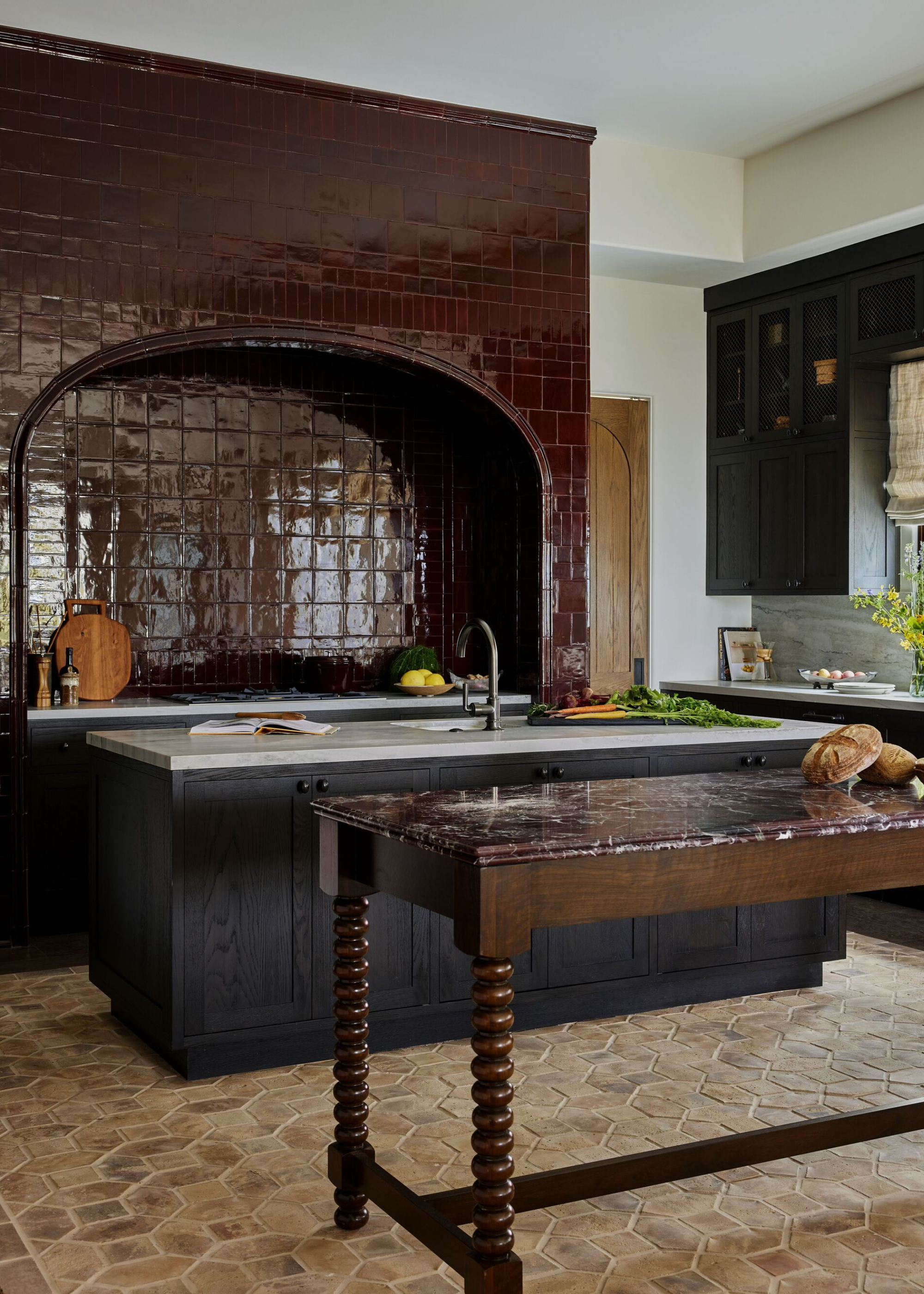 A kitchen with a glossy red tiled hood and a portable kitchen island in the middle of the kitchen as well as a standard island next to it