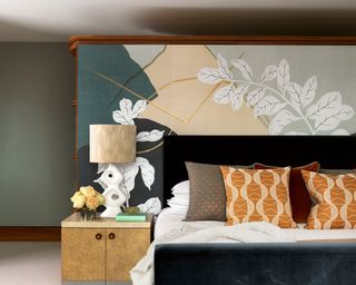 A black bed with orange patterned cushions and a floral wall mural behind