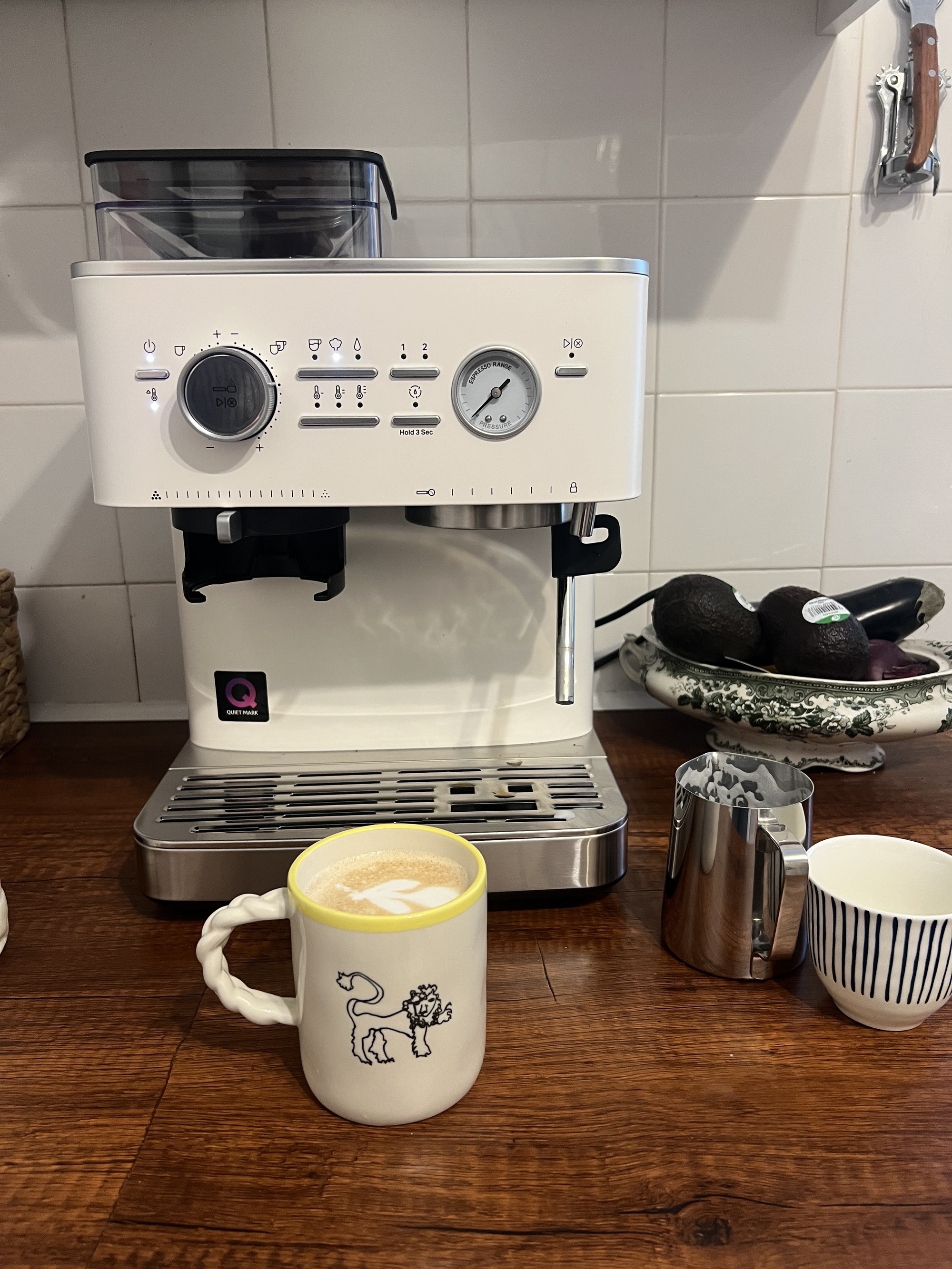 Image of a white KitchenAid coffee machine on a wooden countertop with a coffee mug that is full of a latte.