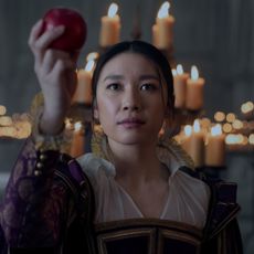 Jin Cheng (Jess Hong) holds up an apple while standing in front of an array of candles, in episode 103 of 3 Body Problem