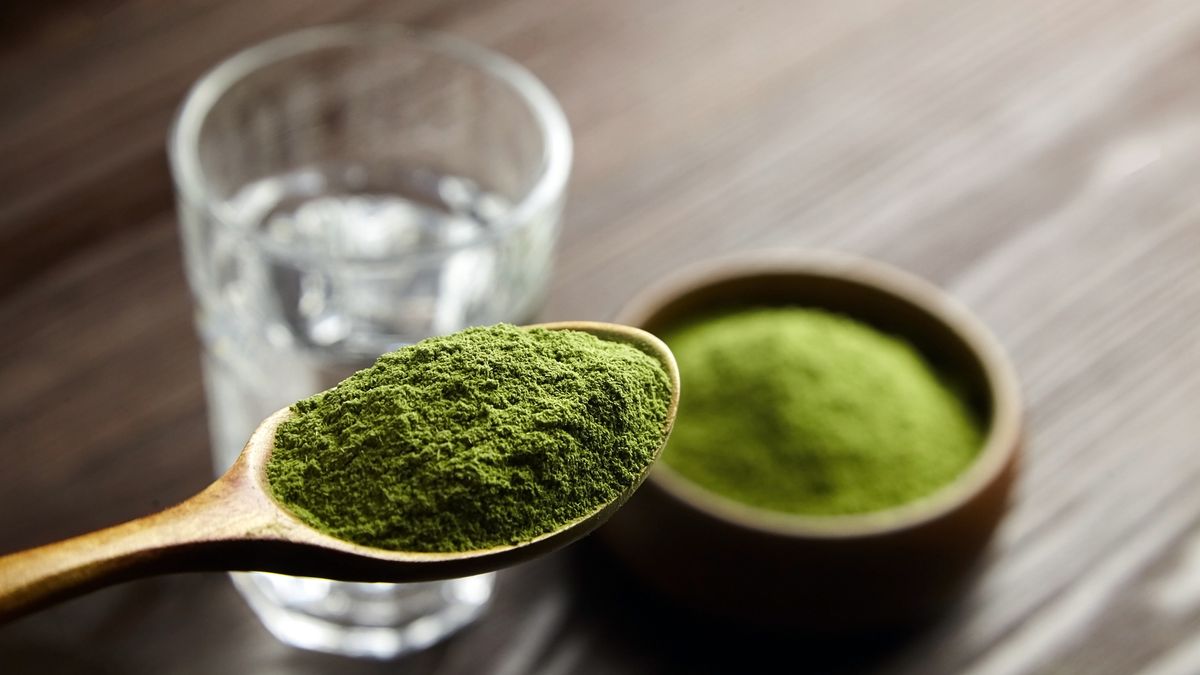 A photo of a teaspoon of a greens powder being held over a glass