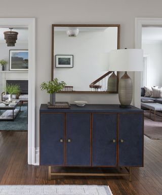 A foyer with a dark blue and brown wood sideboard, large mirror and views into two living rooms