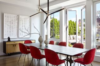 A mid century modern style dining room with large wooden table, red chairs and statement lighting fixture