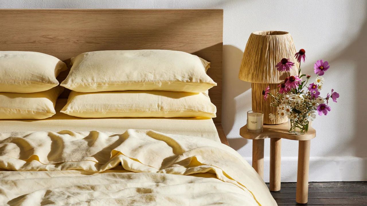 Limoncello linen sheets on a bed against a white wall beside a wooden nightstand with pink flowers.