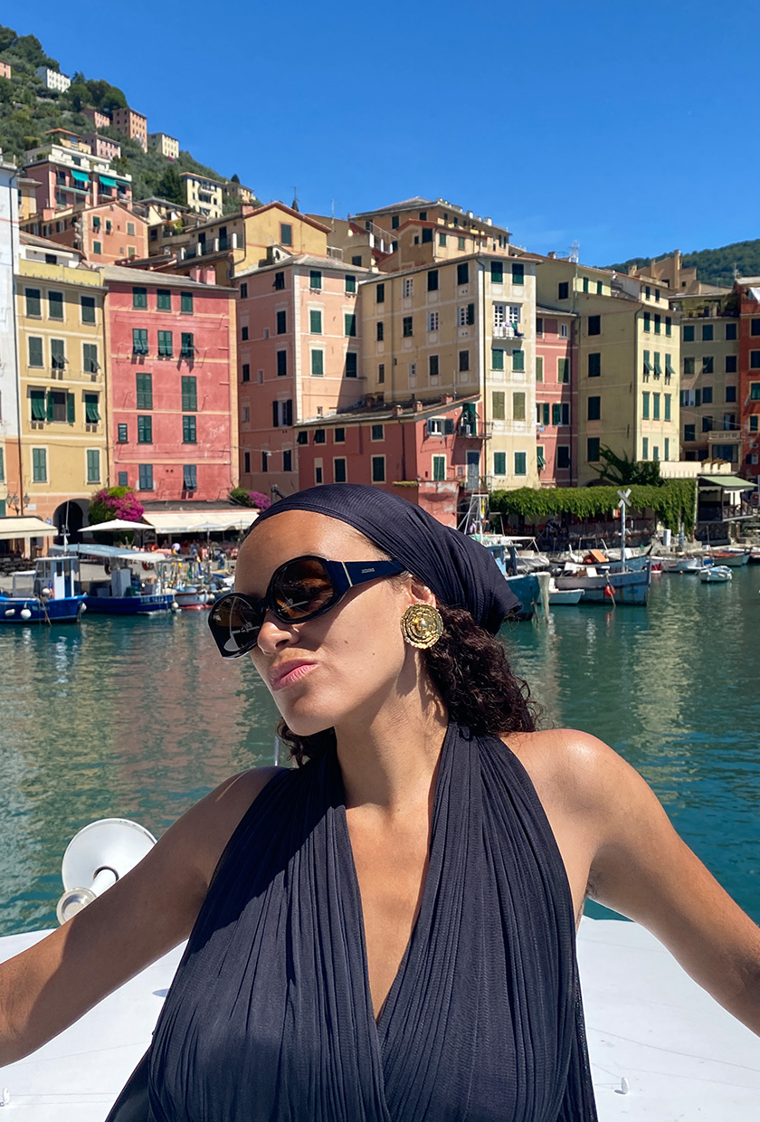 How to pack for Italy is shown in a close picture of a fashion editor wearing a black headscarf, black halter, gold earrings and oversized sunglasses