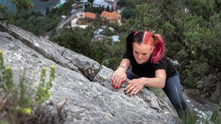 Dexterous girl teenager gripping a stone wall with her hands climbing up a steep cliff 