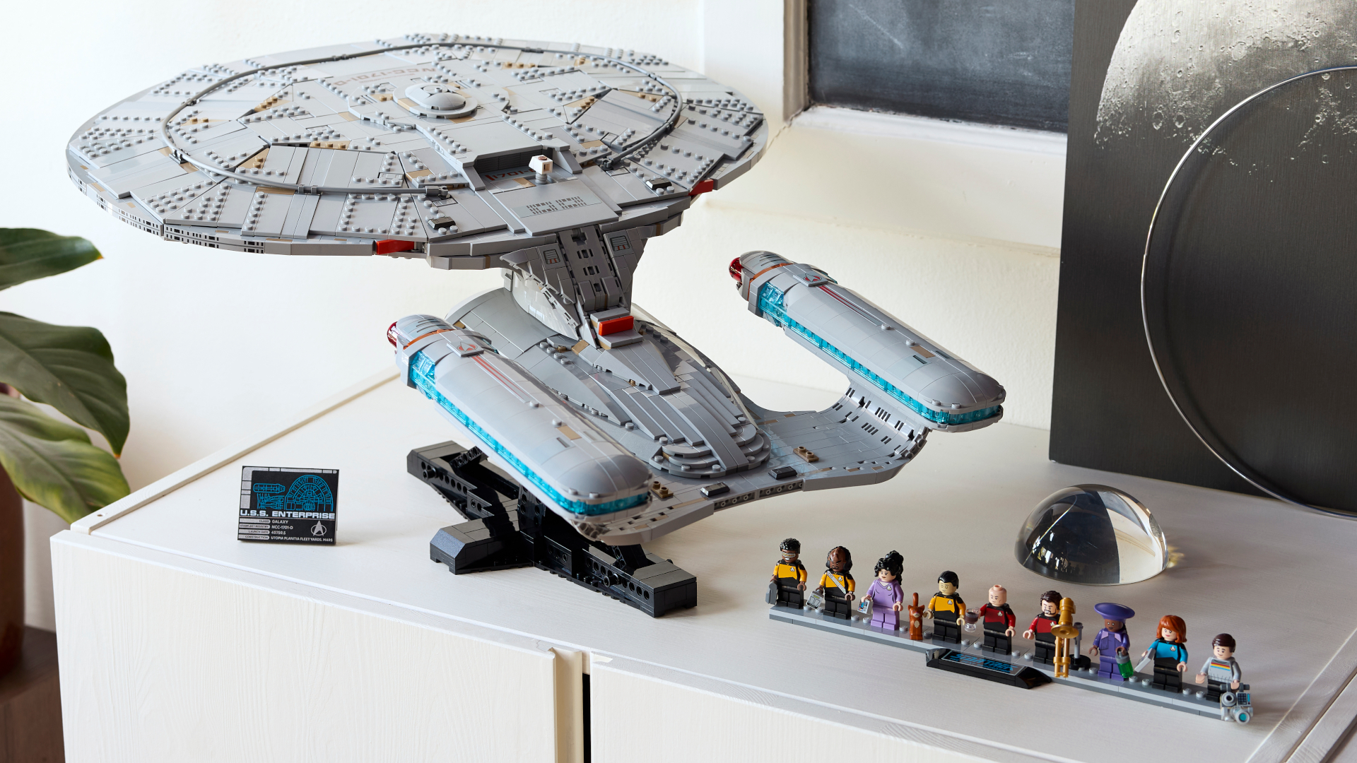 Lego Enterprise and minifigures on a white surface, with artwork of a moon in the background