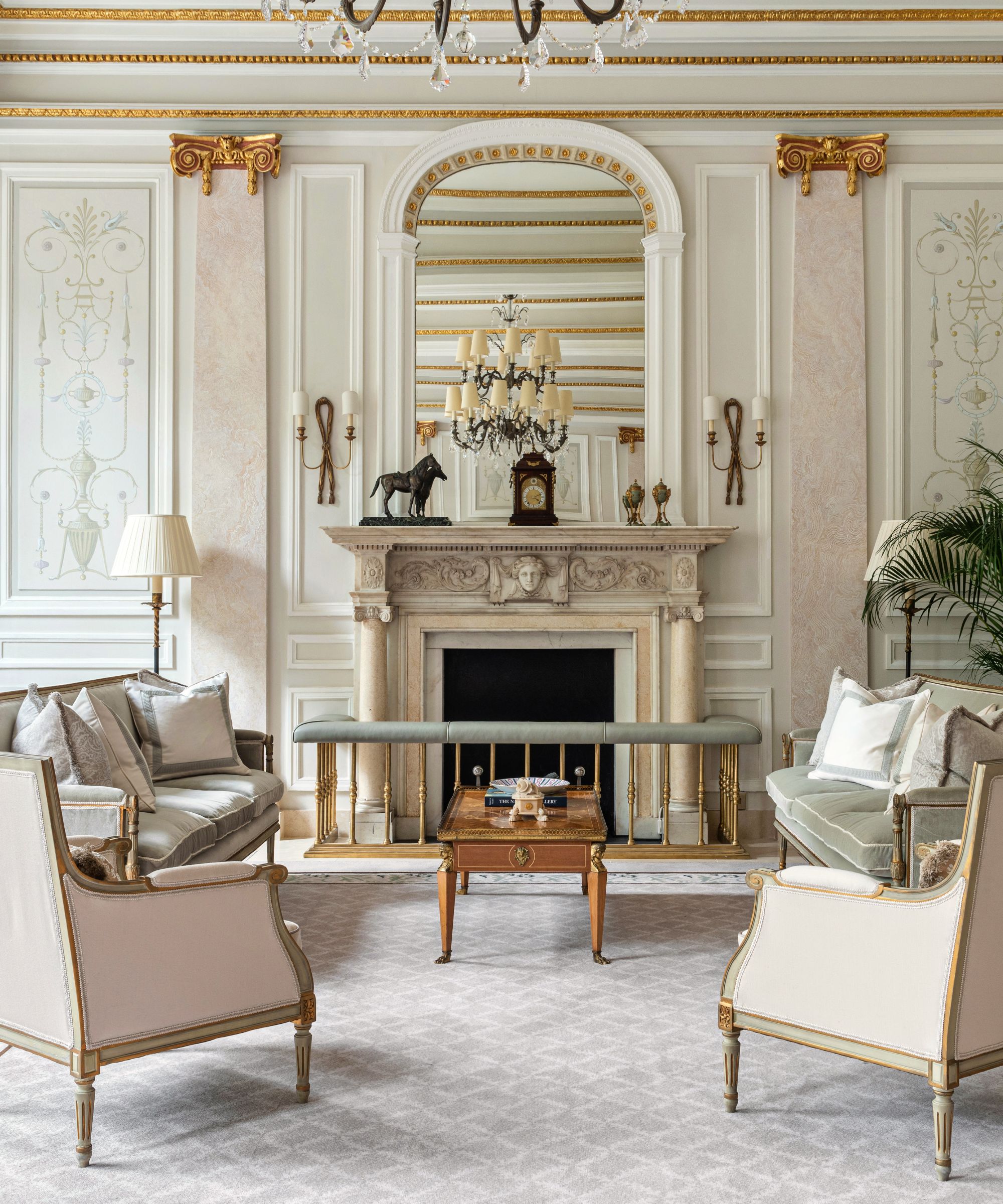 regency style neutral gray and pink drawing room with an antique fireplace, fender, blue gra rug, formal settees with armchairs all facing each other