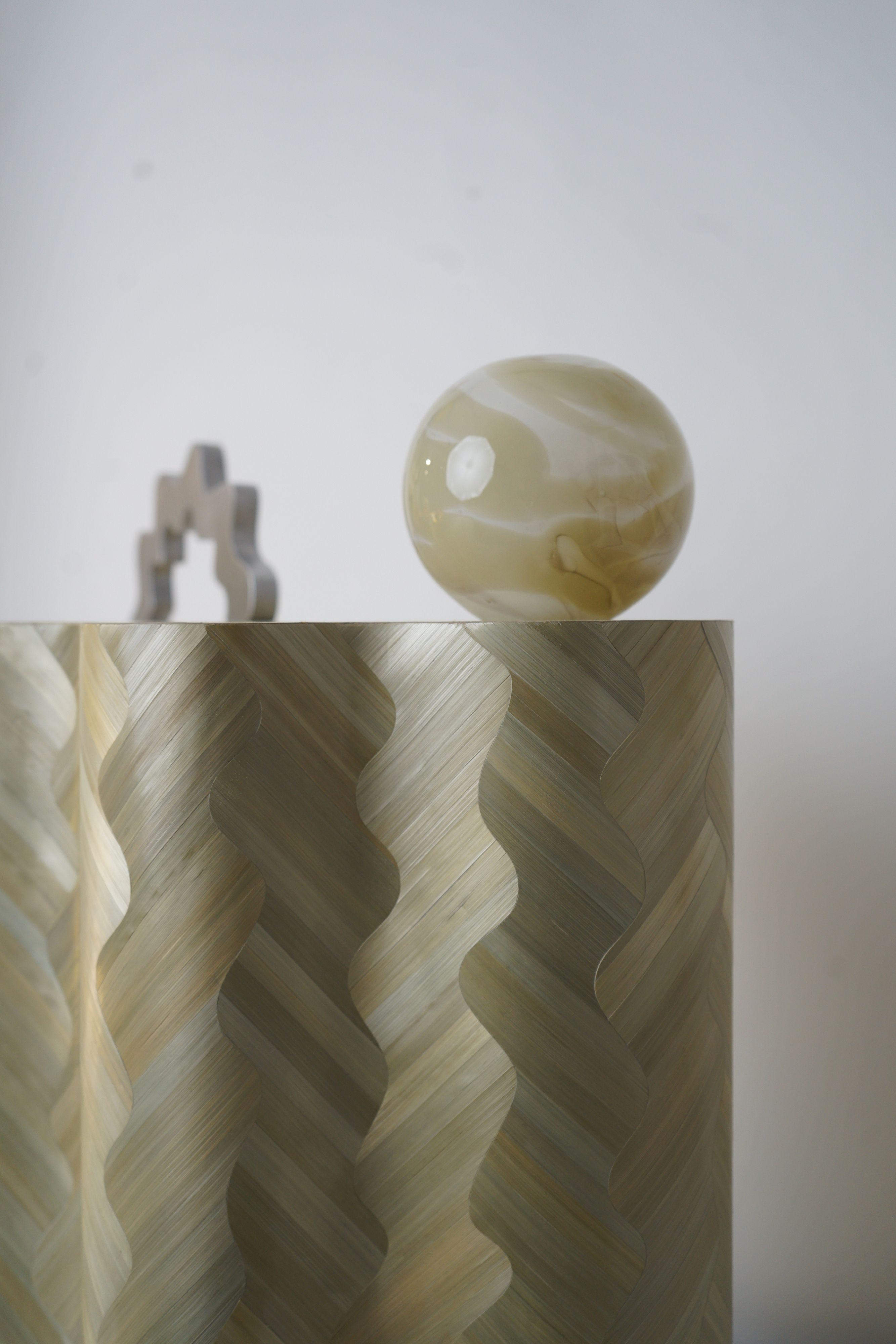 A close-up of a polished stone and natural fiber sculpture made of wavy patterns and a earth-like globe, positioned on its top right side.