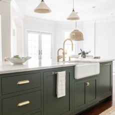 green kitchen with Benjamin Moore Vintage Vogue, white countertops, pendant lights, a butlers sink with gold tap, white fruit bowl, gold hardware, and white walls
