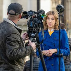 Rhiannon Mills in a blue coat standing in front of a cameraman