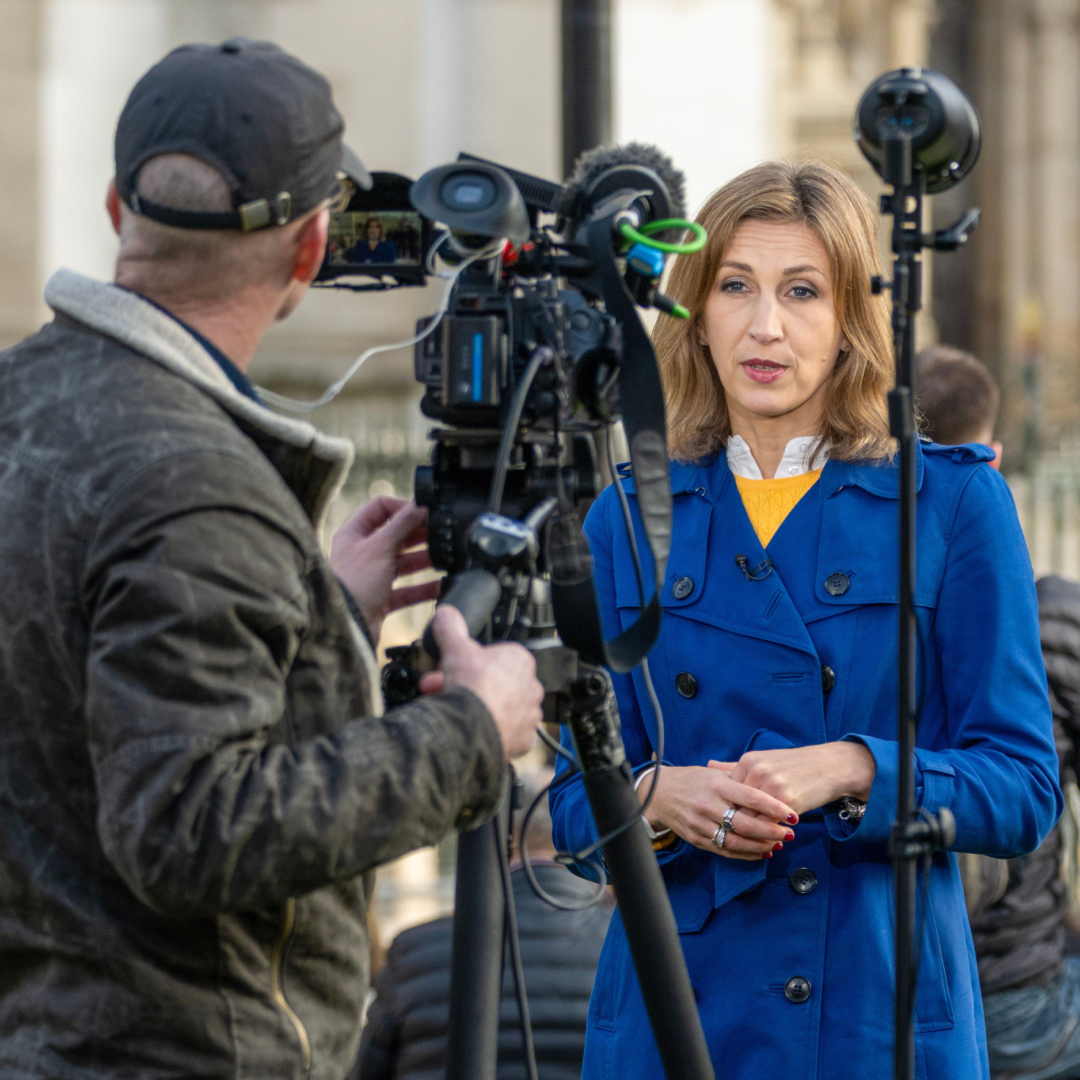 Rhiannon Mills in a blue coat standing in front of a cameraman