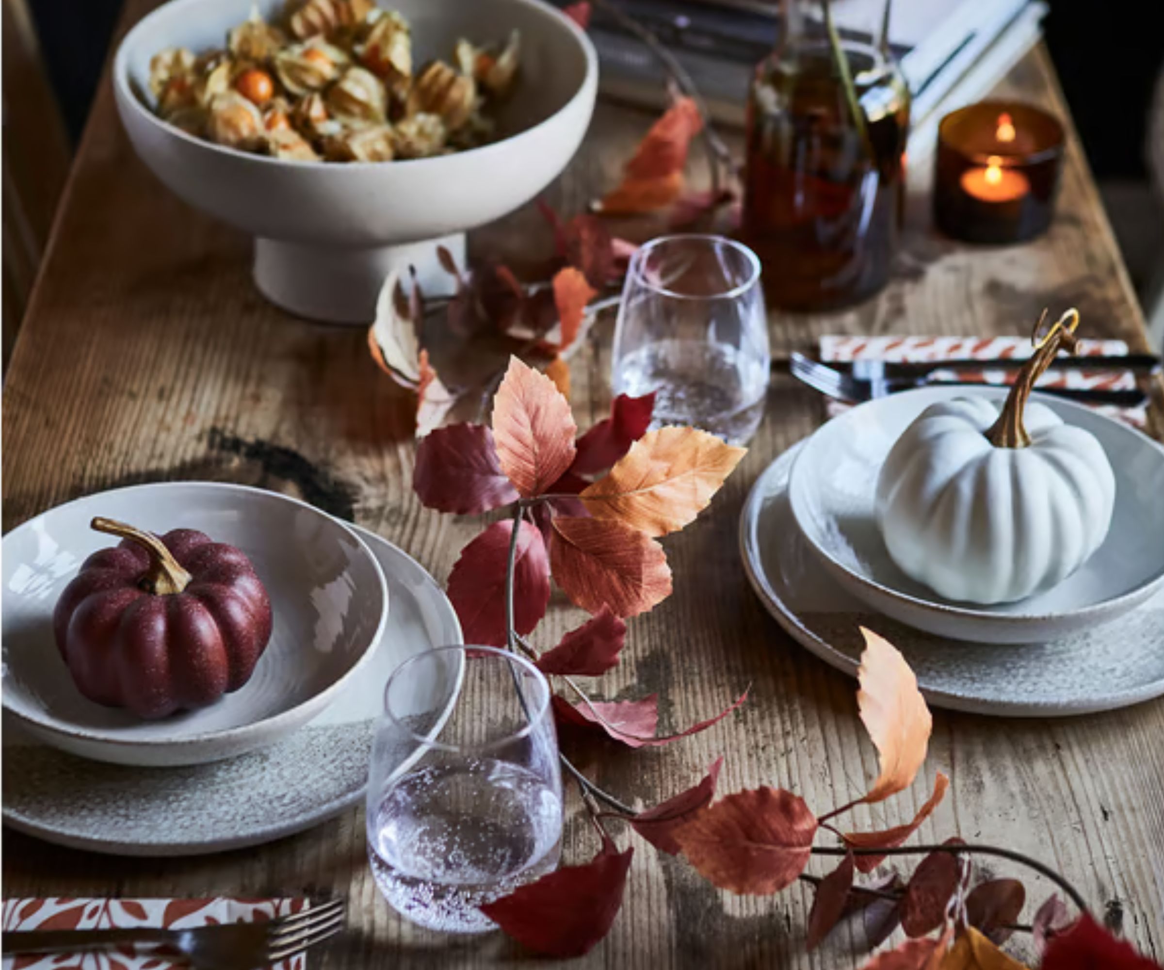 Wood table with white ceramic plates and bowls, leaf garland, tumblers and tealights and pumpkins