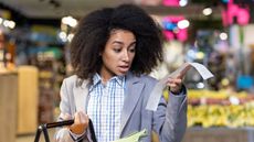 A shopper looks surprised as she looks at her receipt in a grocery store.