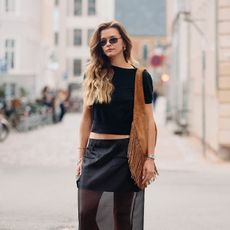 Woman wears black tee, black semi sheer skirt, large suede shoulder bag, and thong kitten heels. 