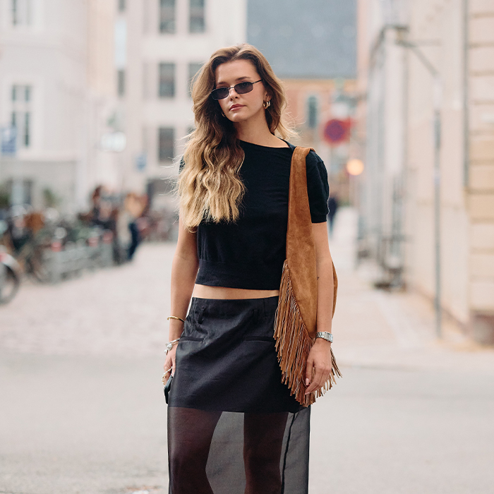 Woman wears black tee, black semi sheer skirt, large suede shoulder bag, and thong kitten heels. 