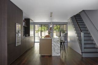 Basement kitchen with handless cabinetry, central island, industrial-style glazing and staircase