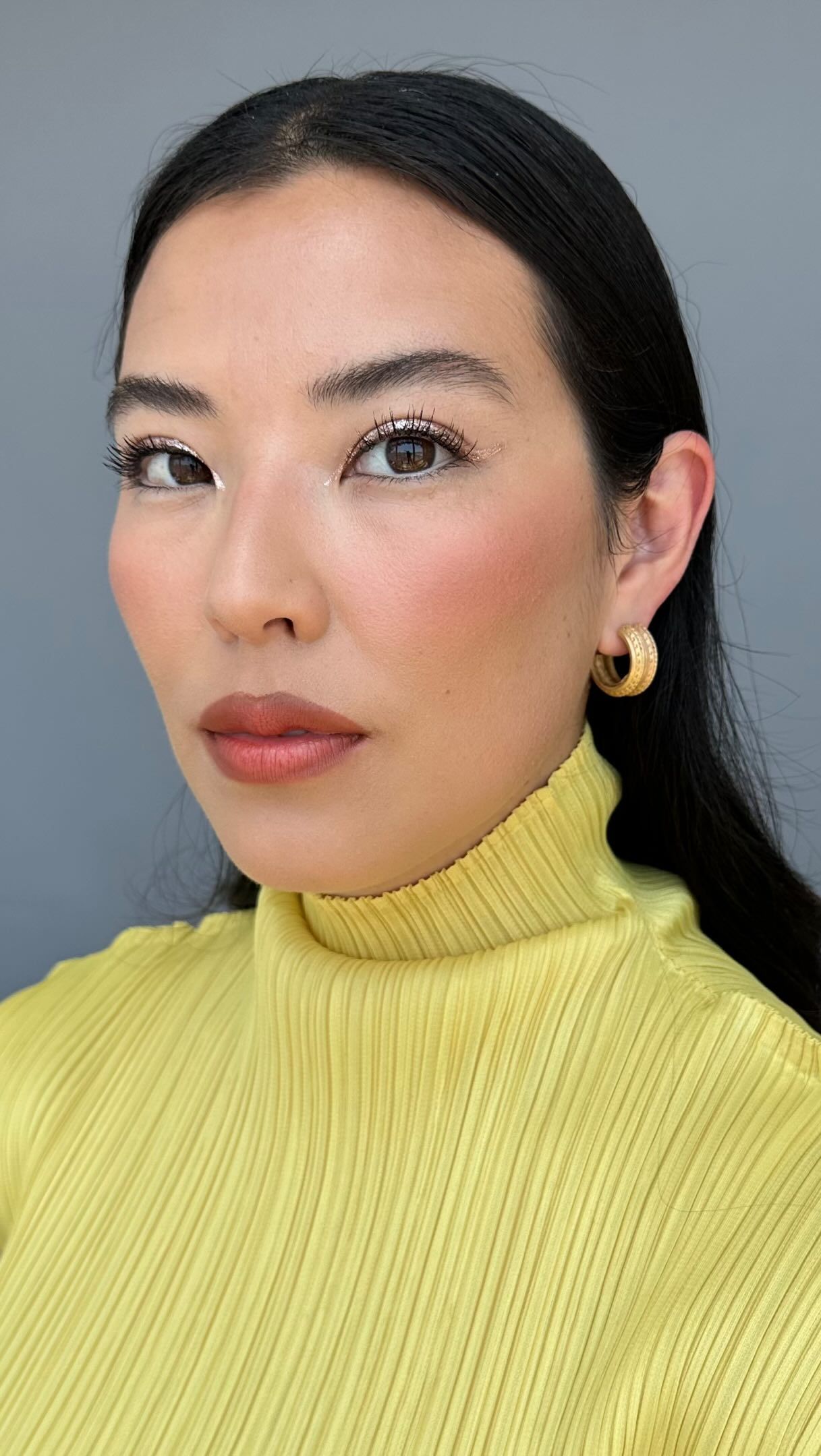 Photo of a woman in a yellow turtleneck wearing gold eye shadow and mascara
