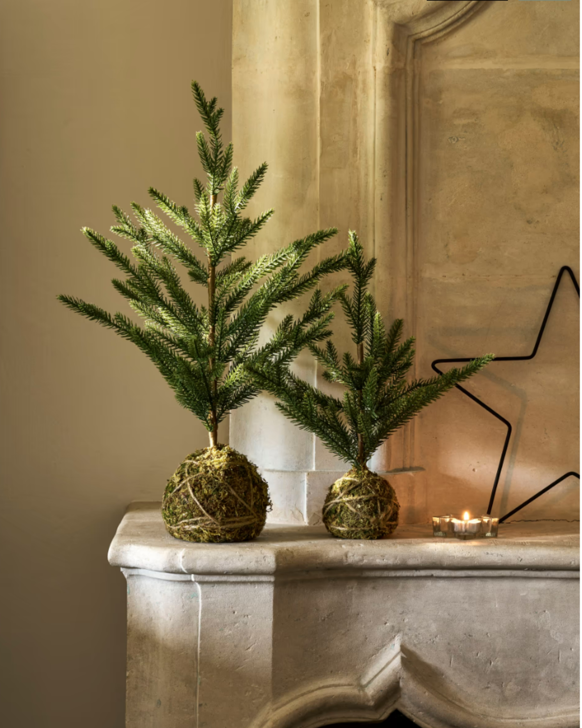 Image of two mini Christmas trees in a moss ball base on a stone fireplace mantel.