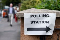 A polling station sign with someone who has been through the register to vote process approaching it (photo by Mike Kemp/In Pictures via Getty Images)
