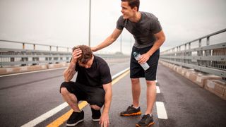 Man consoles runner crouched down with hand on head