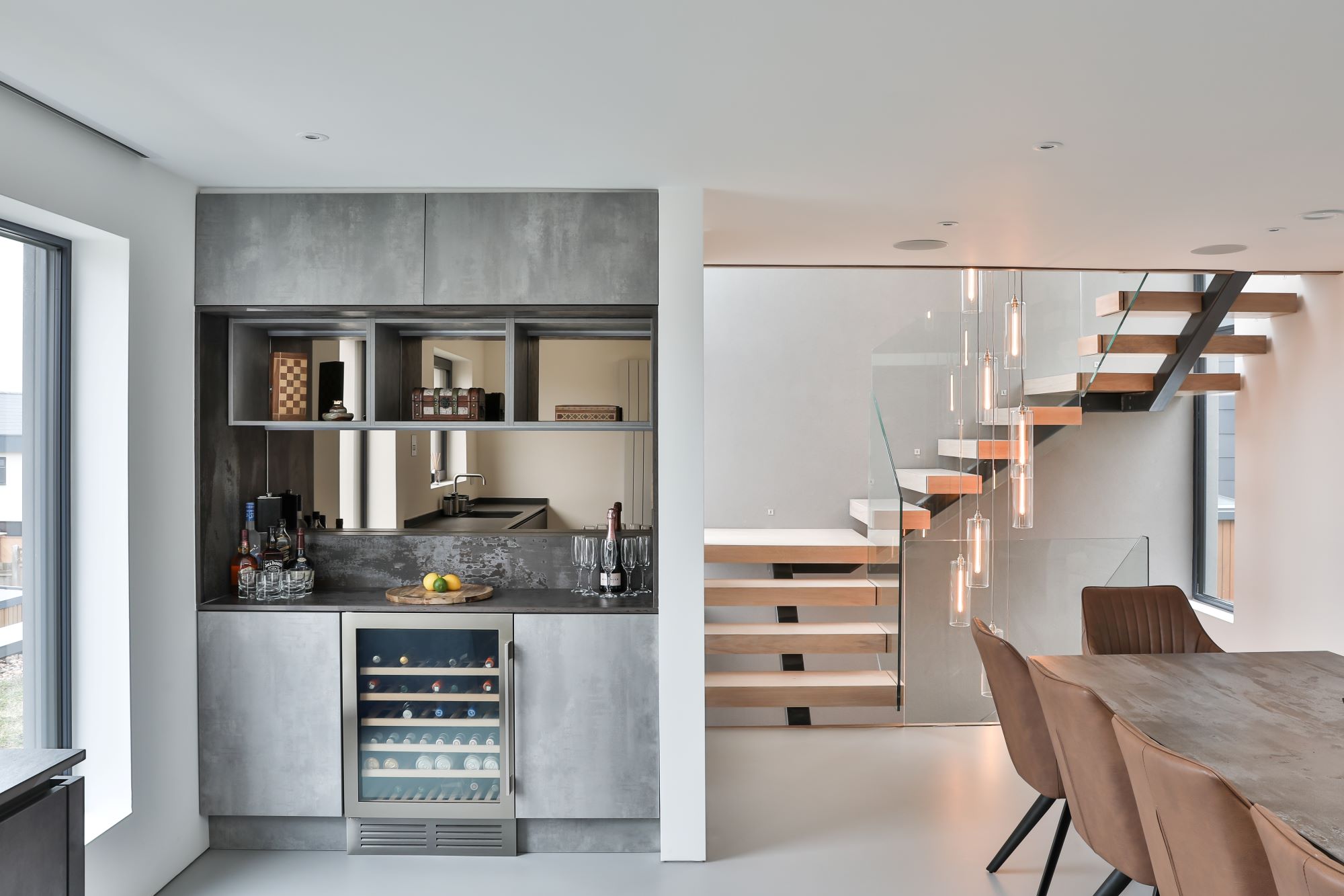 The living room shows a book shelf and a wooden stair case with glass walls
