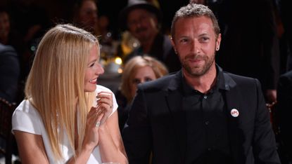 Gwyneth Paltrow and Chris Martin smile together sat at a table.